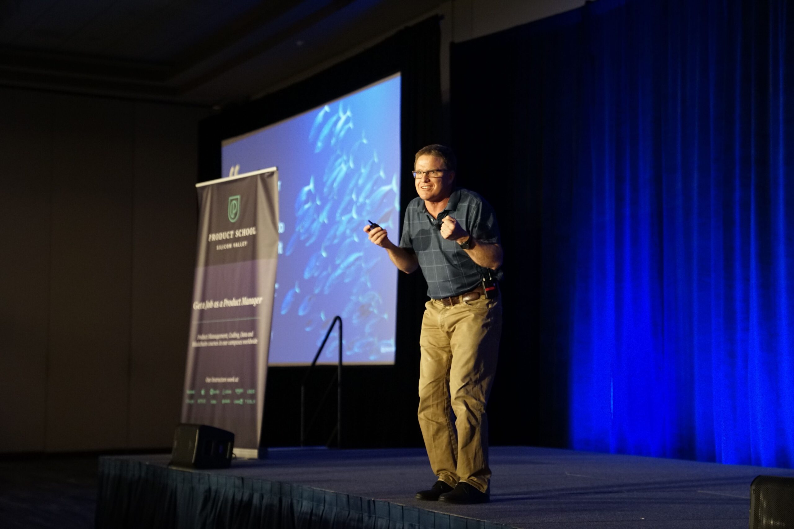 Man onstage with a screen behind him giving a presentation at a conference.